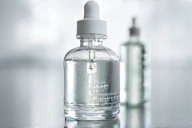 A clear glass bottle of serum with a dropper